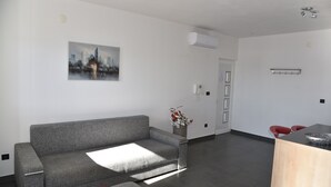 A modern living room with a grey sofa, a red chair, a wooden coffee table, and a cityscape painting on the wall. - Villa Pina TOP****Apartment Nicos at the see 2-4 persons (Tisno)