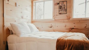 A wooden cabin bedroom with a bed, a window, and a wall-mounted artwork.