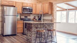 A kitchen with wooden cabinets, a stainless steel refrigerator, a built-in oven, a microwave, a stone island with bar stools, and a window providing natural light.
