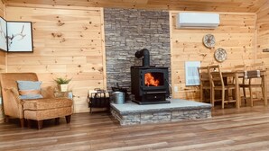 A cozy cabin interior with a stone fireplace, wooden walls, a dining area, and a comfortable seating area.
