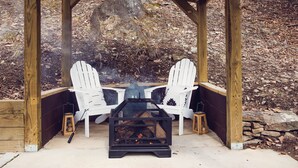 A wooden gazebo with two Adirondack chairs and a wood-burning stove.