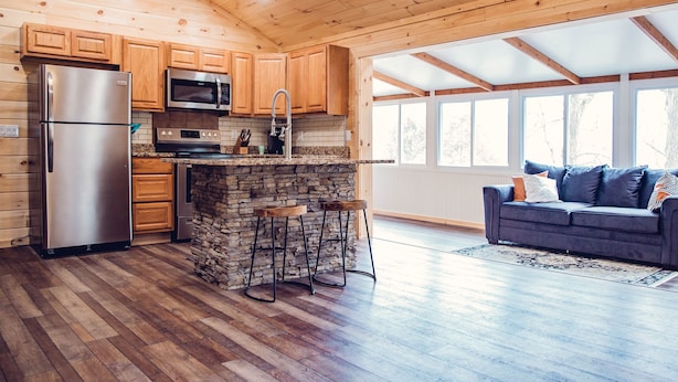 A modern kitchen with wooden cabinets, a stone island, and a stainless steel refrigerator.