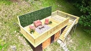 Une terrasse en bois avec des meubles d’extérieur, un escalier et une haie verdoyante.