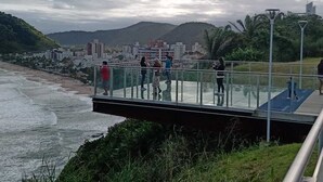 Eine Glasbrücke über einem Strand mit einer Stadtlandschaft im Hintergrund.