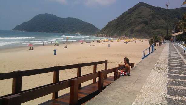 Ein Strand mit einer Holzpromenade, Sand und einem Berg im Hintergrund.