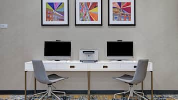 A hotel room with a desk, two chairs, and three framed artworks on the wall.