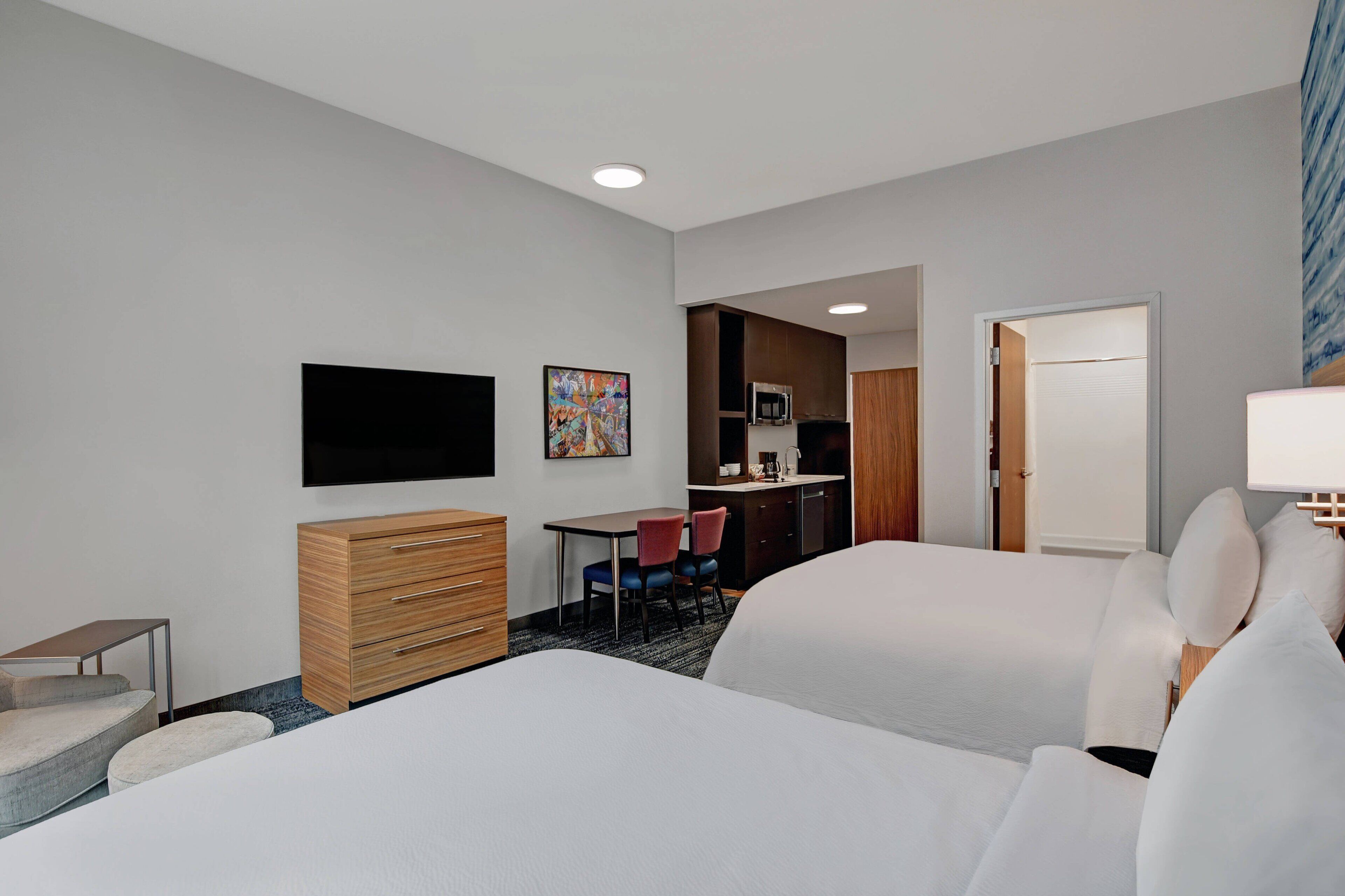 Habitación de hotel con dos camas, un escritorio, una silla, un aparador, un televisor y un microondas.