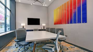 A conference room with a large table, six chairs, two lamps, a flat-screen TV, and a colorful wall art piece.