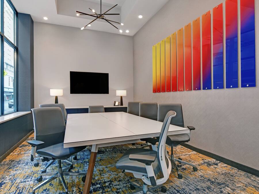 A conference room with a large table, six chairs, two lamps, a flat-screen TV, and a colorful wall art piece.