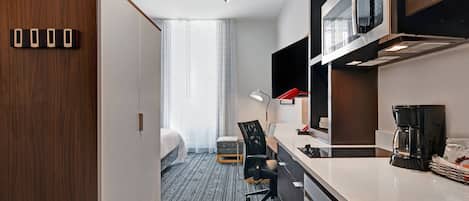 A compact hotel room with a kitchenette, a bed, a desk, and a chair.