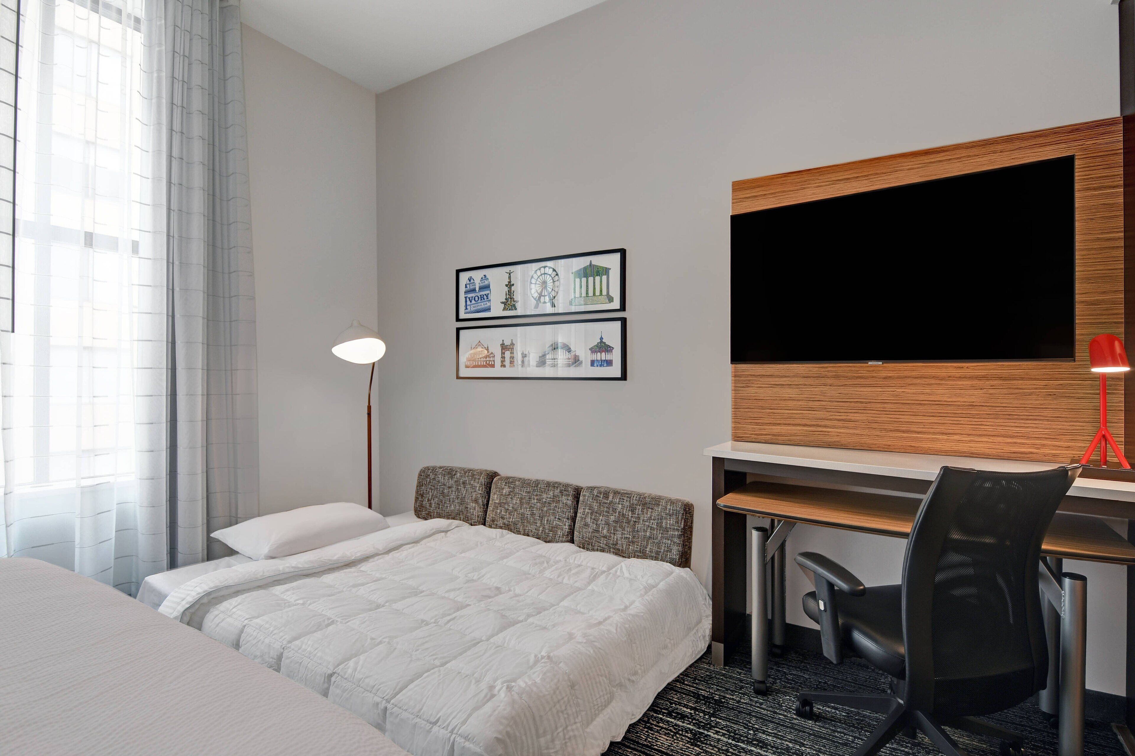 A hotel room with a bed, desk, chair, and a flat-screen TV.