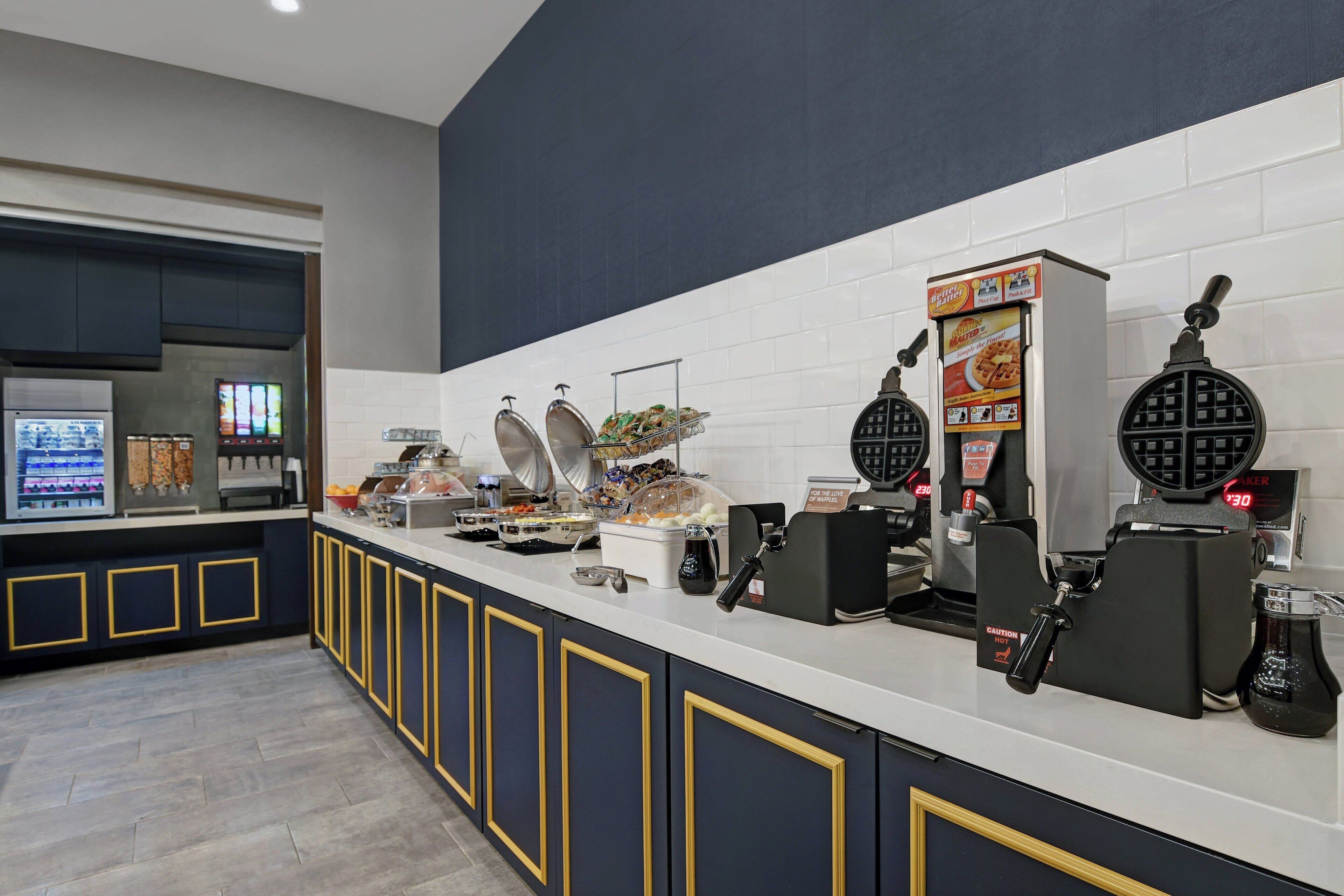 Un banco buffet con diverse postazioni gastronomiche, tra cui macchine per waffle e una macchina del caffè.