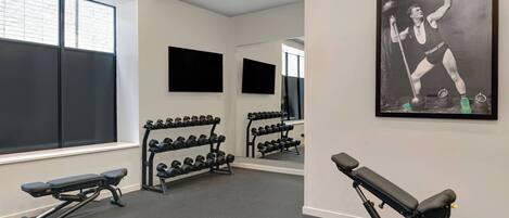 A gym with benches, dumbbells, and a large mirror.