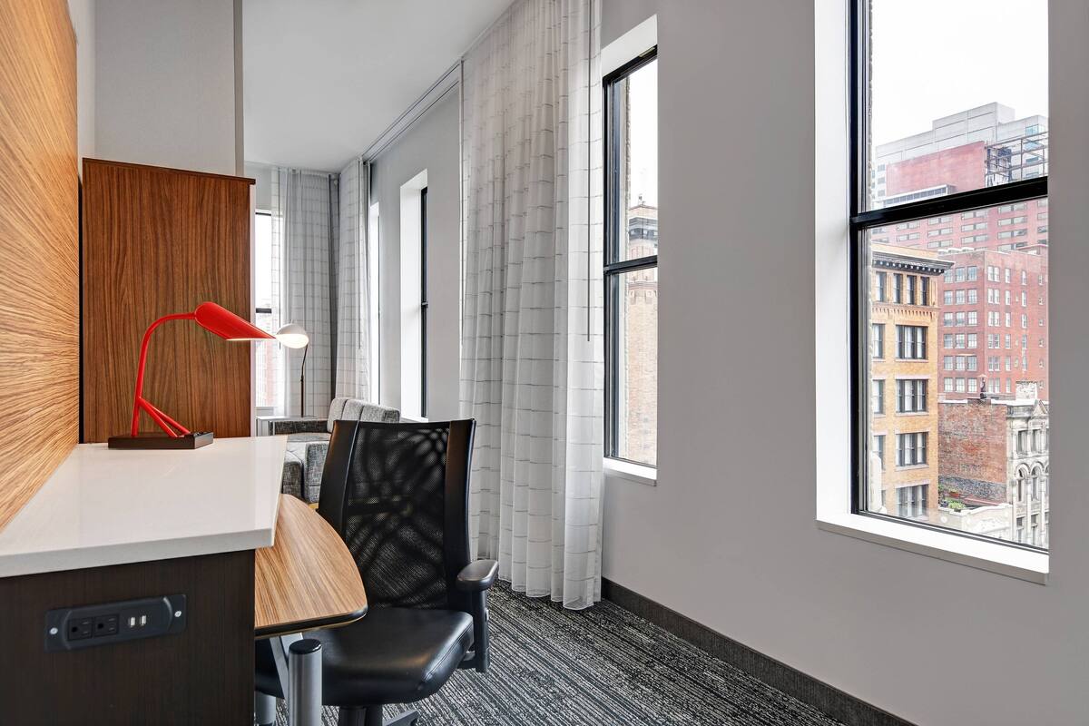 Une chambre d’hôtel équipée d’un bureau, d’une chaise et d’une grande fenêtre donnant sur la ville.