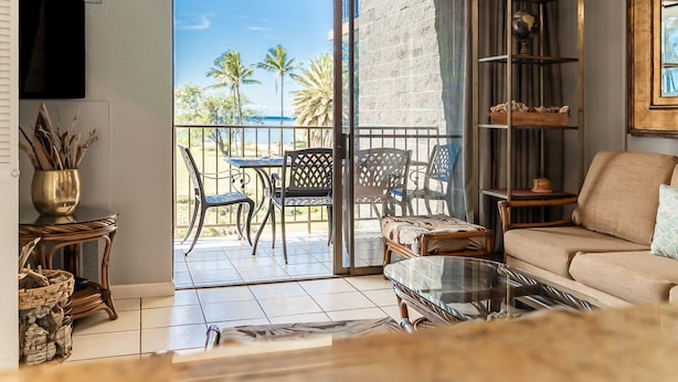 A living room with a sofa, a glass coffee table, and a balcony with outdoor furniture.