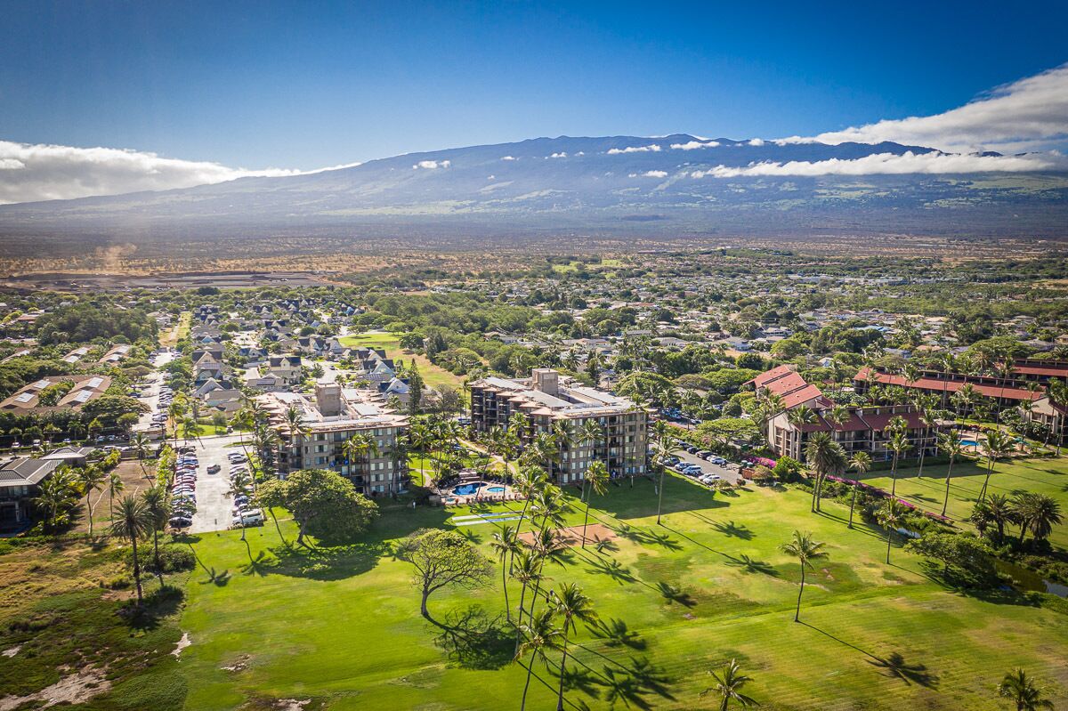 An aerial view of a resort with multiple buildings, a swimming pool, and a lush green landscape.