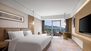Habitación de hotel con una cama grande, un escritorio, una silla, un televisor y vistas a las montañas.