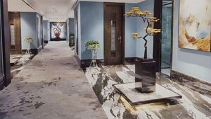 Pasillo de hotel con suelo de mármol, una obra de arte central y una planta en maceta.