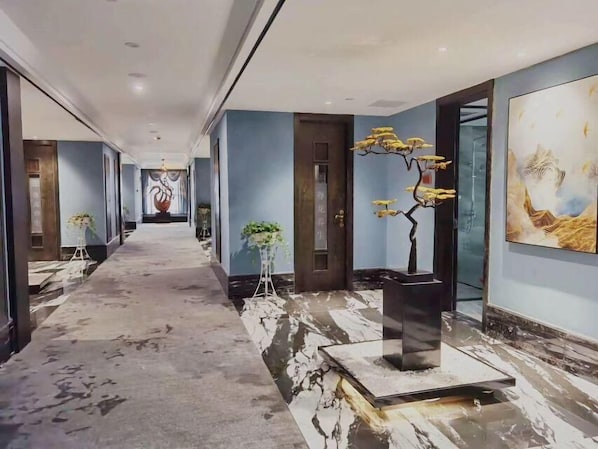 Een hotelgangen met marmeren vloer, een kunstwerk in het midden en een potplant.