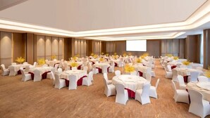 Un amplio salón de conferencias con varias mesas redondas, sillas blancas y arreglos florales amarillos.