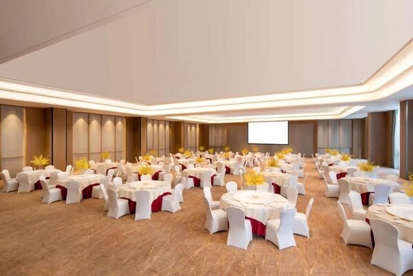 A large conference room with multiple round tables, white chairs, and yellow flower arrangements.