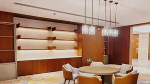 Habitación de hotel moderna con una mesa redonda, cuatro sillas, alfombra estampada, paneles de madera e iluminación colgante.