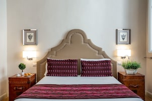 Une chambre d’hôtel avec un grand lit, deux tables de chevet, une tête de lit et deux lampes fixées au mur.