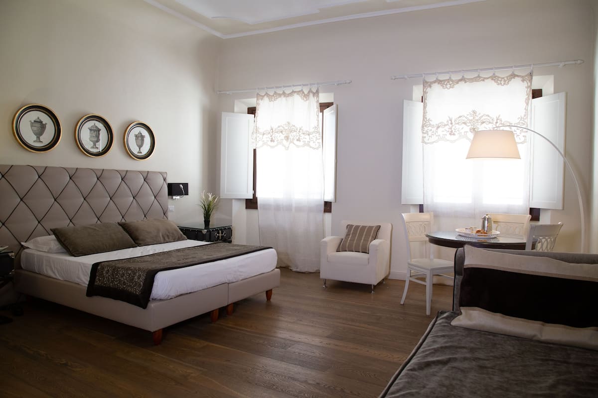 A bedroom with a bed, bedside table, lamp, chair, and a small table with a lamp.