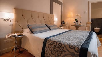A neatly made bed with a patterned bedspread, a bedside table with a lamp, and a small table with a vase of flowers.