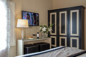 Een hotelkamer met een bed, een aan de muur bevestigde televisie, een bureau met een lamp, een bloemenvaas en een kledingkast.