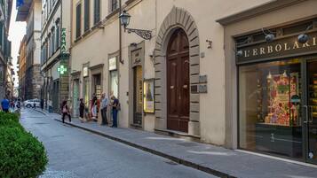 Una strada con negozi, tra cui una farmacia e un negozio chiamato L'Erboliari.