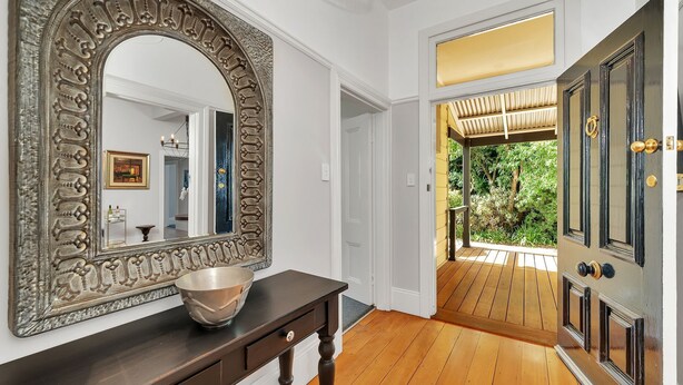 A hallway with a large ornate mirror, a wooden console table with a bowl, and a door leading to a covered outdoor area.