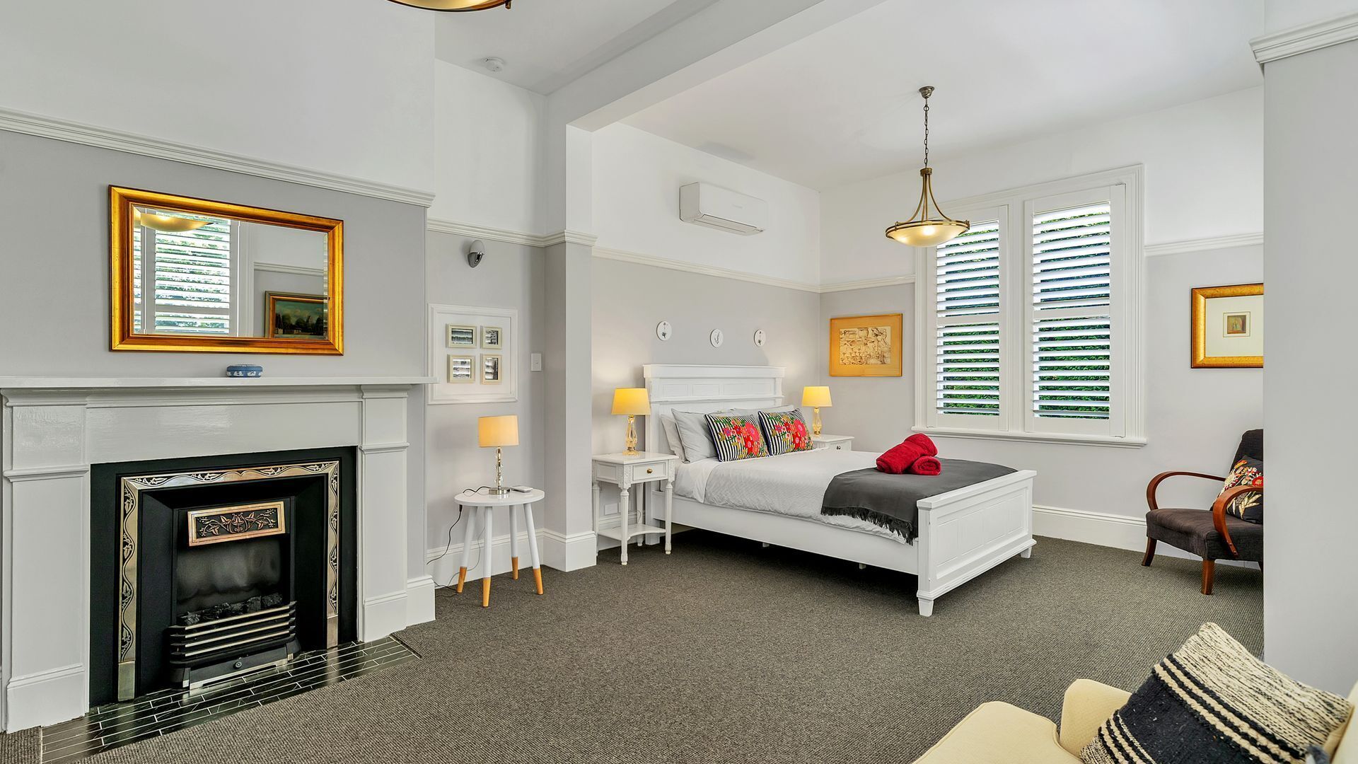 A bedroom with a fireplace, a bed with a red towel, a chair, and a window with blinds.