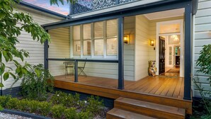 A covered porch with a wooden deck, a table and chairs, and a door leading to the interior.