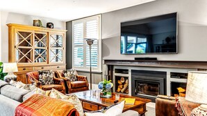A living room with a fireplace, a large flat-screen TV mounted above it, and a wooden cabinet with glass doors.