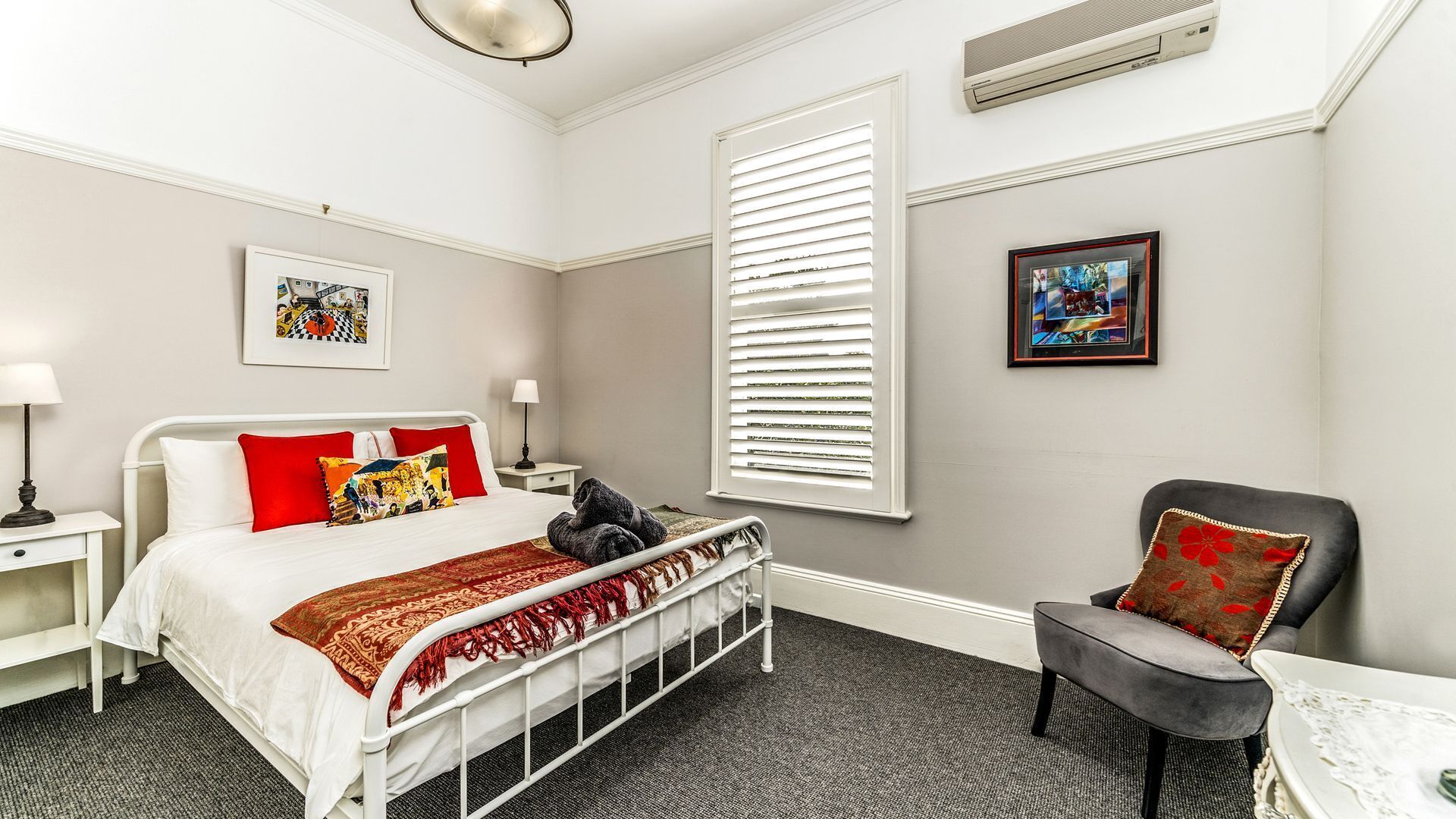 A hotel room with a bed, a chair, a desk, a window with blinds, and a picture on the wall.