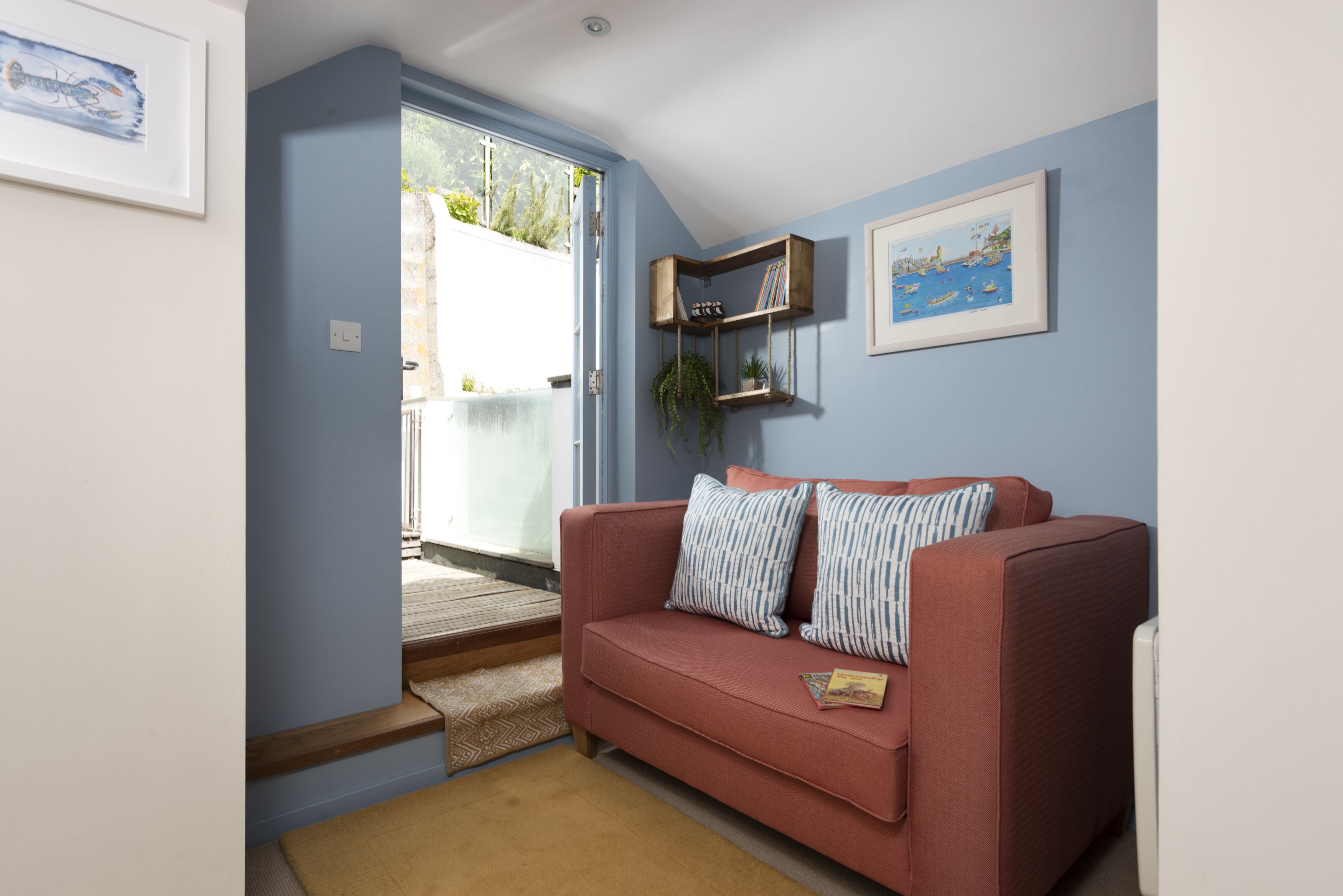 Una sala de estar con un sofá rojo, una estantería de madera con plantas y un cuadro en la pared.