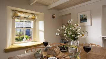 A dining table with a loaf of bread, cheese, olives, and a vase of flowers.