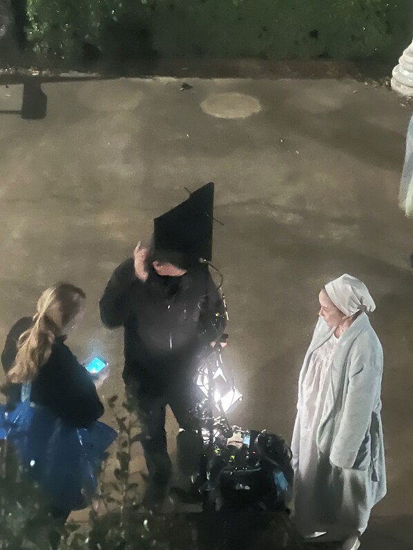 A nighttime outdoor scene with a person in a graduation cap and gown standing next to a vehicle. - Above the Law (Natchez)