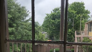 Een balkon met een houten hekwerk, een witte tafel en stoelen, en uitzicht op een achtertuin met bomen en een bakstenen gebouw.