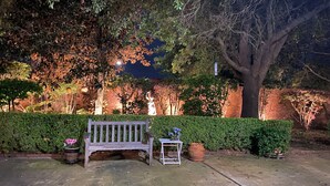 Een bank en tafel in een tuin met een haag en bomen.
