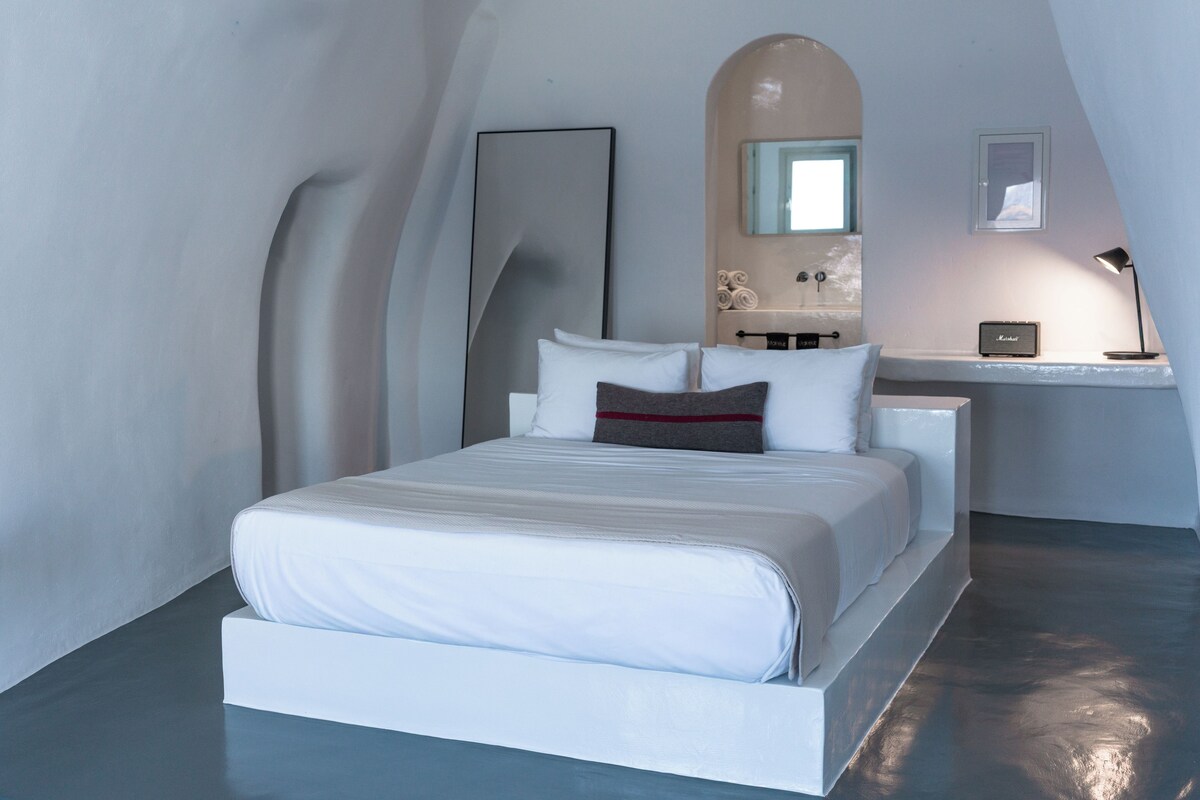 Un dormitorio moderno con cama, mesita de noche, lámpara, espejo y vista al cielo.