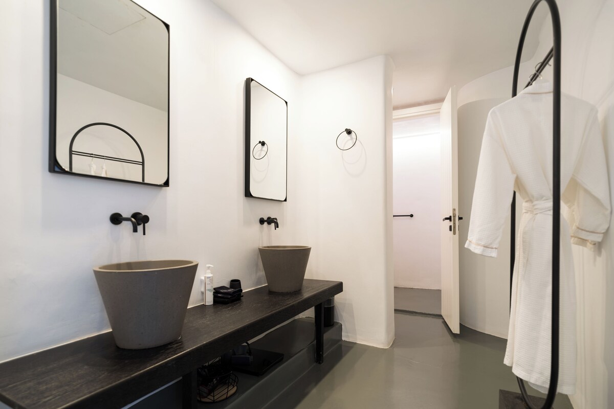 Un baño moderno con dos lavamanos grandes, un espejo y una bata colgada en un perchero.