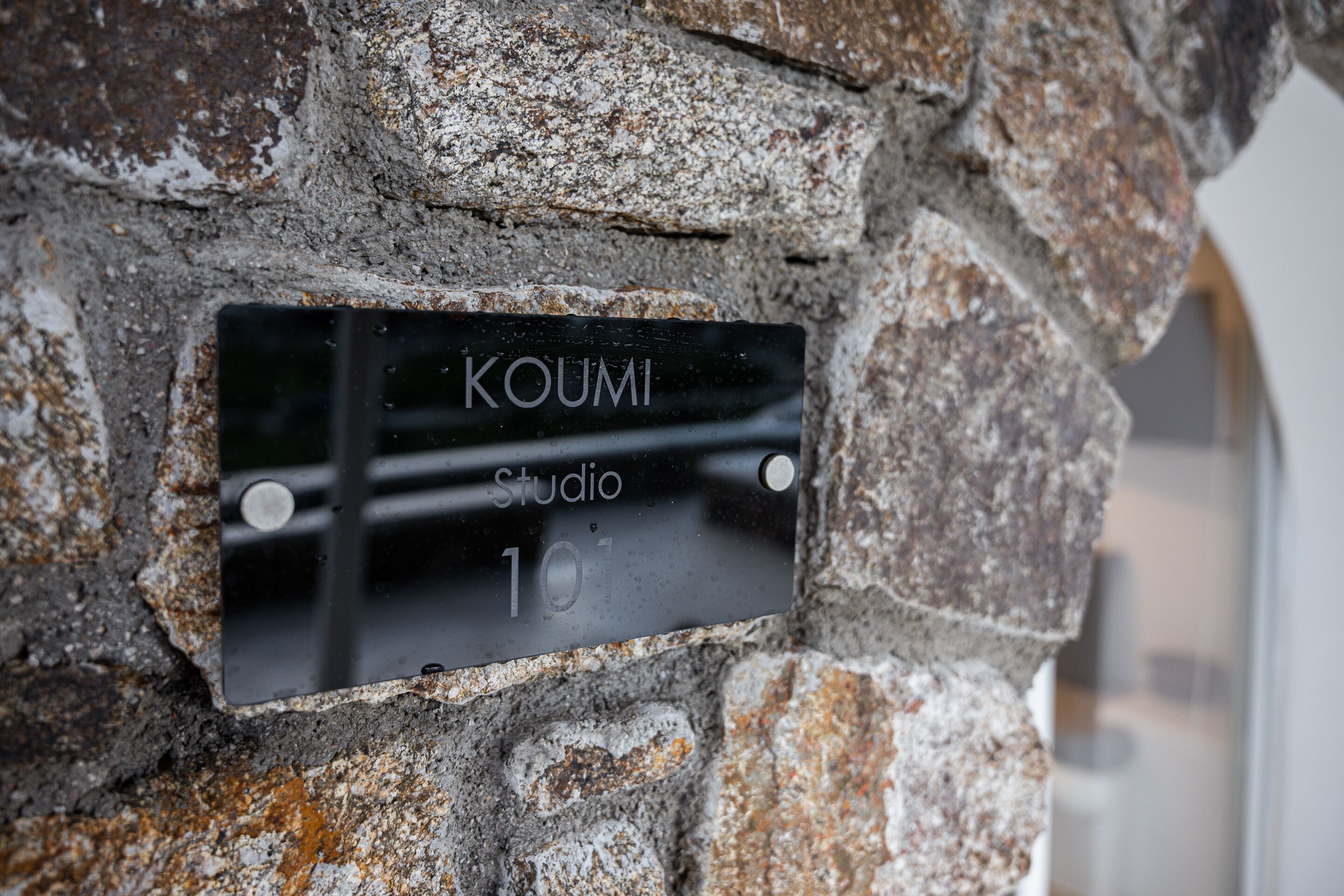 A black metal plaque with the inscription 'KOUMI Studio 101' mounted on a stone wall.