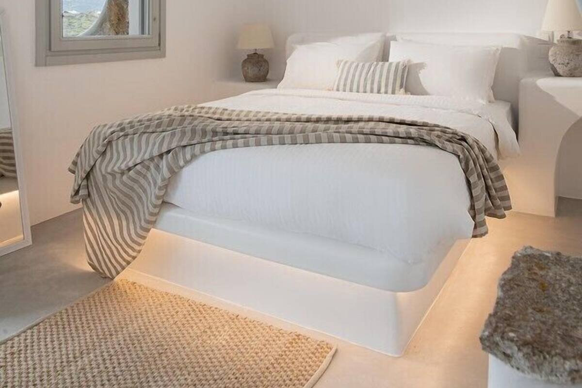 A bedroom with a large bed, a stone wall, a window, and a lamp.