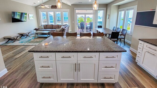 Een ruime keuken met een centraal eiland, witte kasten en een eethoek met een grote tafel en stoelen.