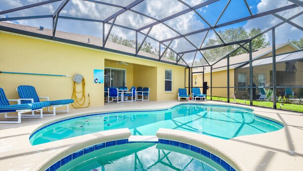Un área de piscina con sillas reclinables azules, un espacio de estar cubierto y una vista despejada del paisaje circundante.