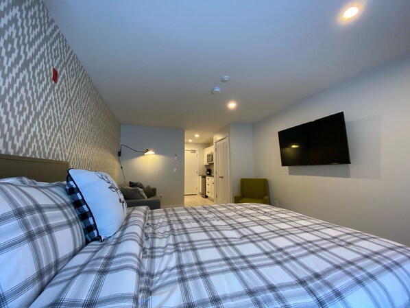 Een slaapkamer met een bed, een aan de muur bevestigde televisie en een behang met patroon.