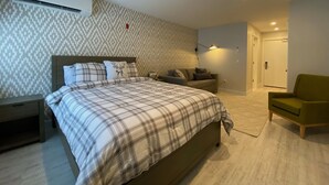 A bedroom with a bed, a nightstand, a sofa, a green armchair, and a patterned wall.