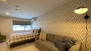 A bedroom with a bed, a sofa, a patterned wall, and a window.